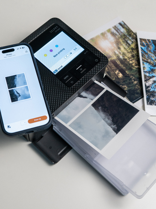 Termosublimační fototiskárna Canon SELPHY CP1500 během tisku fotografie hor, na displeji svítí stav Now printing