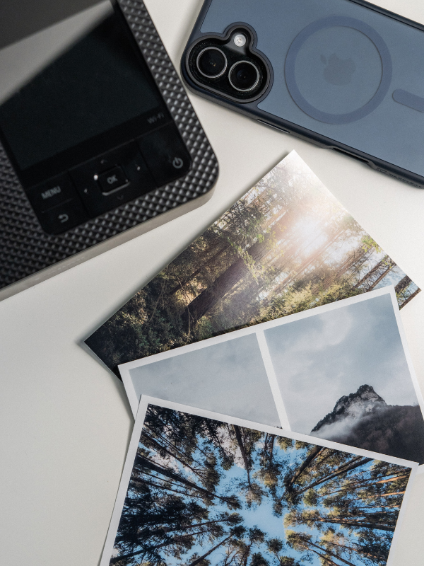 Detailní pohled na tři hotové vytištěné fotografie z přírody s věrnými barvami položené vedle mobilního telefonu a tiskárny