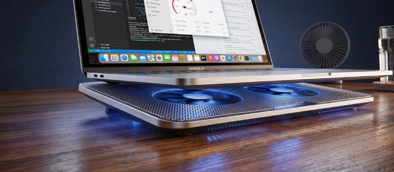 Stříbrný notebook umístěný na aktivní chladicí podložce s modrým podsvícením