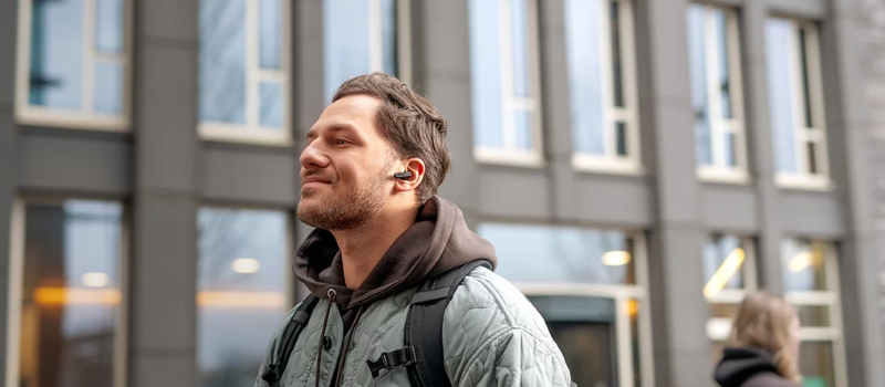 Muž kráčející po městě s bezdrátovými peckovými sluchátky Philips TAT2139 v uchu